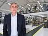 Mann i dress foran moderne lager med høye reoler fulle av esker.