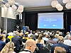 Møtesal fylt av deltakere som følger en presentasjon på lerret merket EC-konferansen.