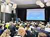 Møtesal fylt av deltakere som følger en presentasjon på lerret merket EC-konferansen.